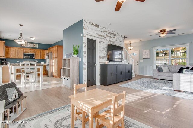 living area with light wood-type flooring, a ceiling fan, and stairs