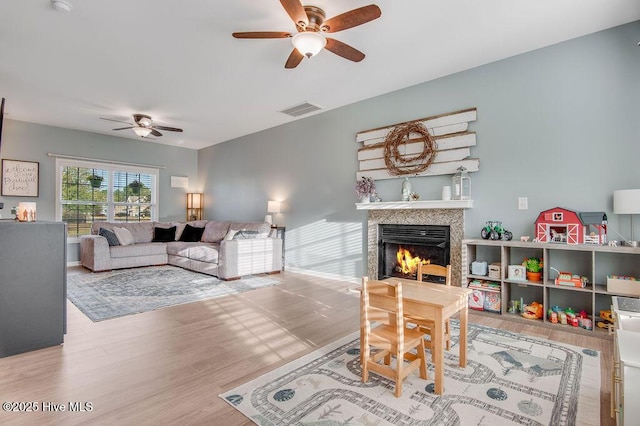 living area with visible vents, a warm lit fireplace, wood finished floors, and a ceiling fan