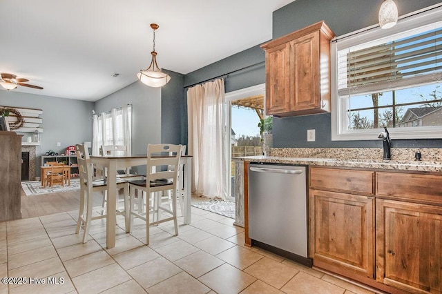 kitchen featuring pendant lighting, a sink, stainless steel dishwasher, a fireplace, and light stone countertops