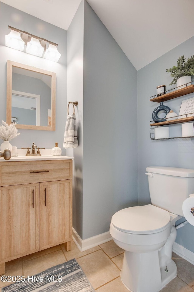 bathroom with baseboards, toilet, vaulted ceiling, tile patterned floors, and vanity