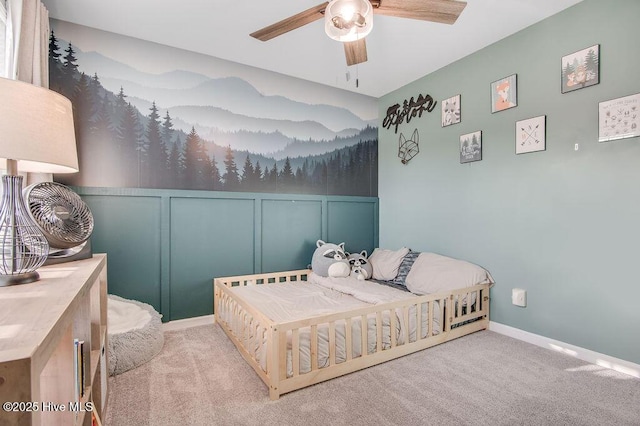 carpeted bedroom with a decorative wall, a ceiling fan, and baseboards