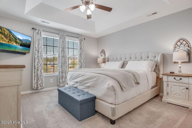 bedroom featuring a tray ceiling, baseboards, light colored carpet, and visible vents