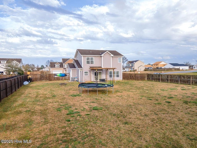 back of property featuring a trampoline, a lawn, a residential view, and a fenced backyard