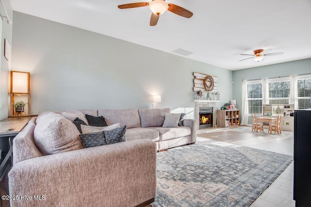 living room with a ceiling fan, visible vents, and a lit fireplace