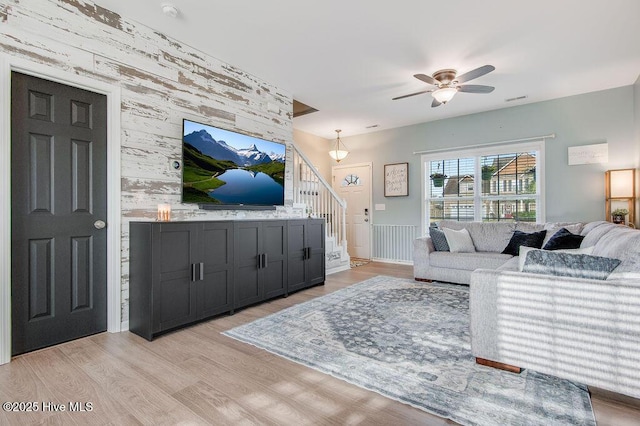 living area with visible vents, an accent wall, ceiling fan, stairs, and light wood-style flooring