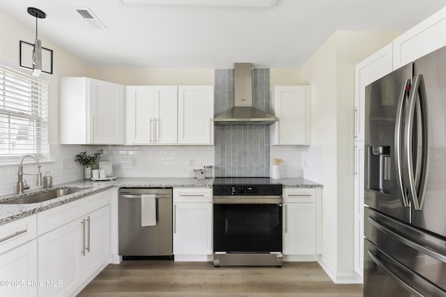 kitchen with visible vents, wall chimney range hood, white cabinets, stainless steel appliances, and a sink