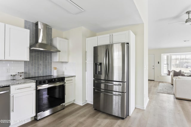 kitchen with light stone countertops, stainless steel appliances, white cabinetry, wall chimney exhaust hood, and backsplash