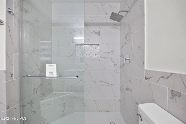 full bathroom featuring toilet, tiled shower, and tile walls