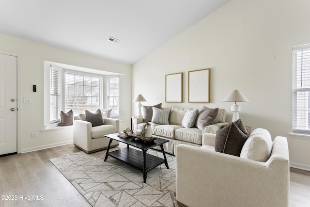 living area with light wood finished floors, visible vents, baseboards, and lofted ceiling