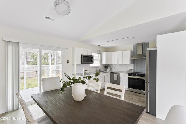 dining space featuring visible vents, light wood-style floors, and vaulted ceiling