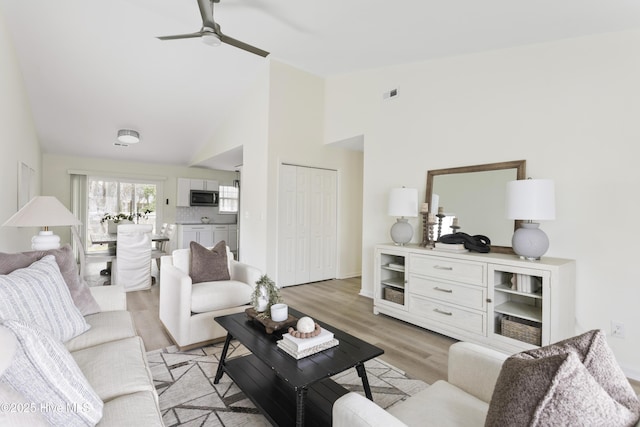 living room featuring high vaulted ceiling, a ceiling fan, visible vents, and light wood-type flooring