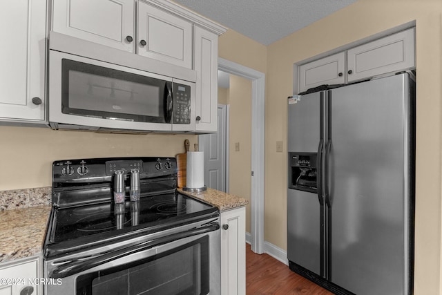 kitchen with a textured ceiling, dark wood-type flooring, light stone counters, and stainless steel appliances