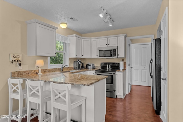 kitchen with dark wood-type flooring, light stone counters, a peninsula, white cabinets, and stainless steel appliances