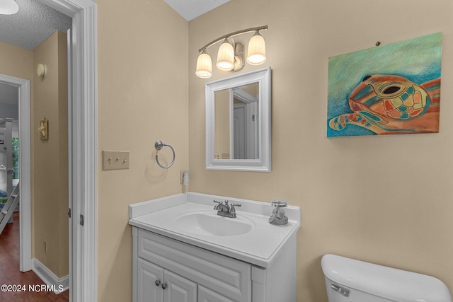 bathroom featuring baseboards, toilet, vanity, wood finished floors, and a textured ceiling