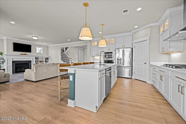 kitchen featuring visible vents, a kitchen breakfast bar, open floor plan, stainless steel appliances, and wall chimney range hood