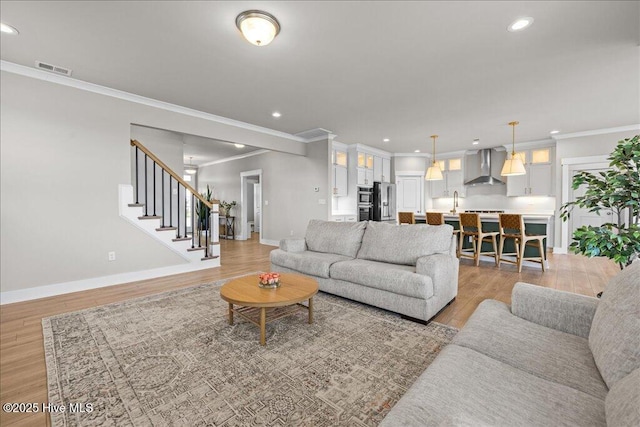 living area featuring light wood-style flooring, stairs, and ornamental molding