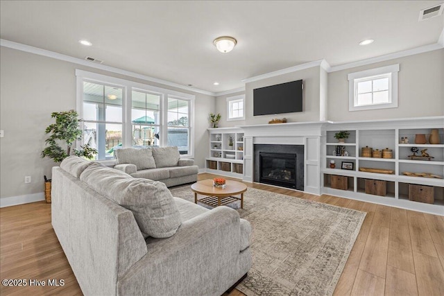 living room with visible vents, wood finished floors, a glass covered fireplace, crown molding, and baseboards