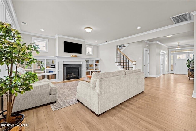 living room featuring a glass covered fireplace, stairs, visible vents, and light wood-type flooring