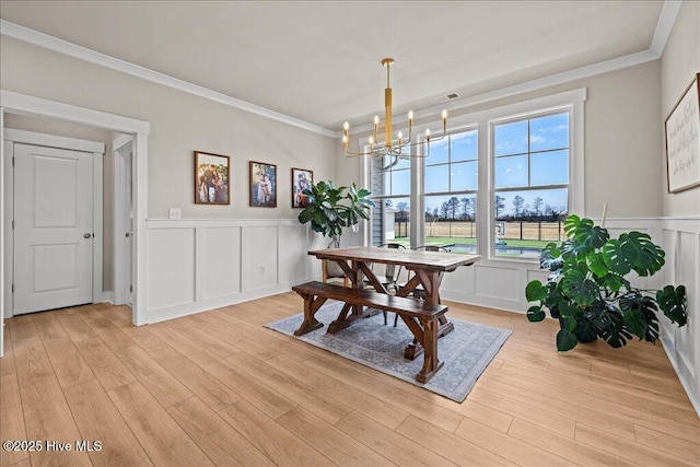 dining space featuring visible vents, an inviting chandelier, light wood-style flooring, crown molding, and a decorative wall