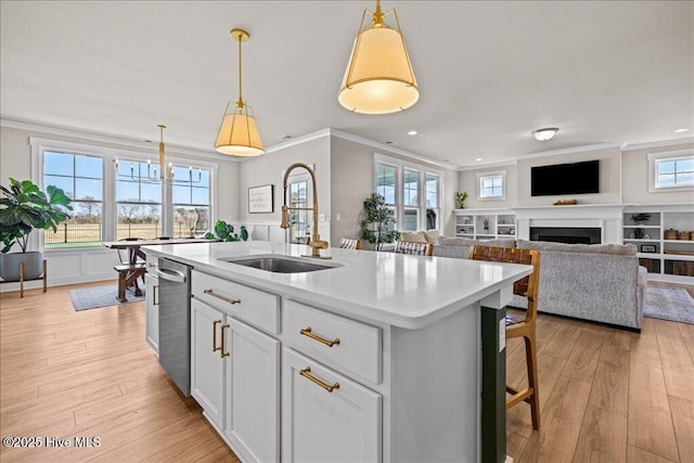 kitchen featuring a sink, stainless steel dishwasher, a fireplace, light countertops, and crown molding