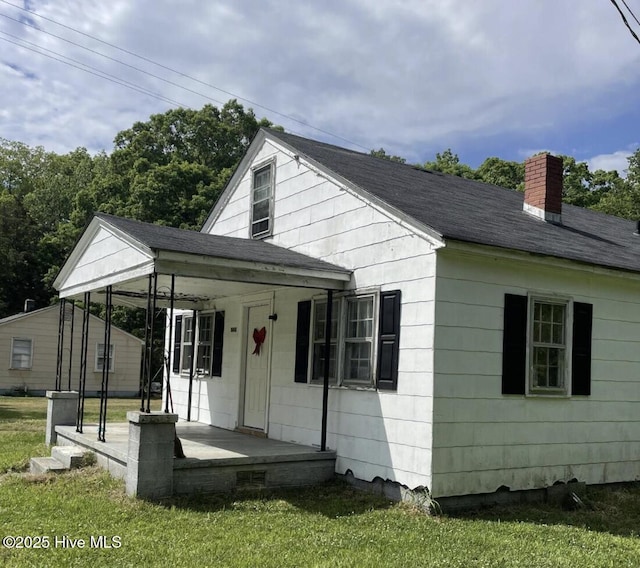 view of front of house featuring covered porch, a chimney, a front yard, and a shingled roof