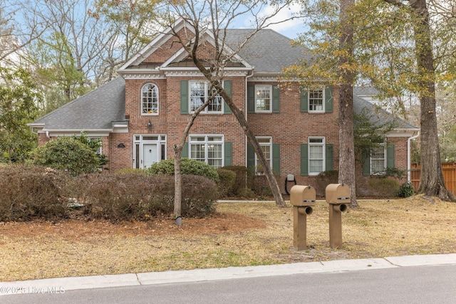 colonial house featuring brick siding and roof with shingles