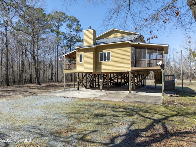 rear view of property featuring stairs, metal roof, a chimney, a sunroom, and driveway