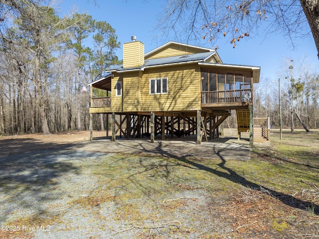 rear view of property featuring stairs, driveway, a sunroom, and a chimney