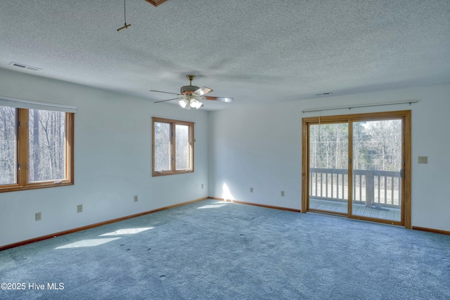 carpeted spare room featuring a wealth of natural light, visible vents, baseboards, and a ceiling fan