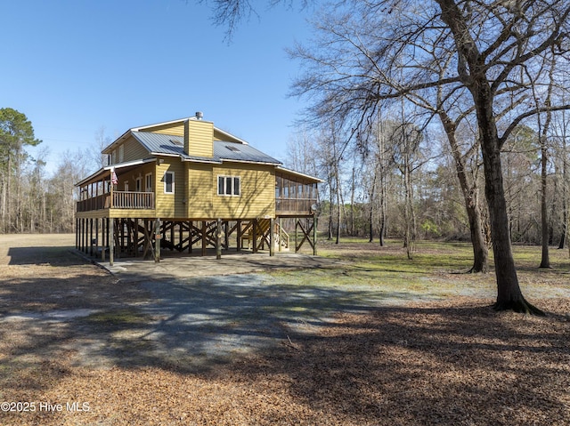 view of property exterior with a carport, a chimney, a deck, and dirt driveway