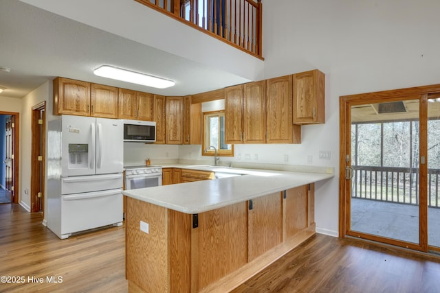 kitchen featuring white appliances, a peninsula, light wood finished floors, and light countertops