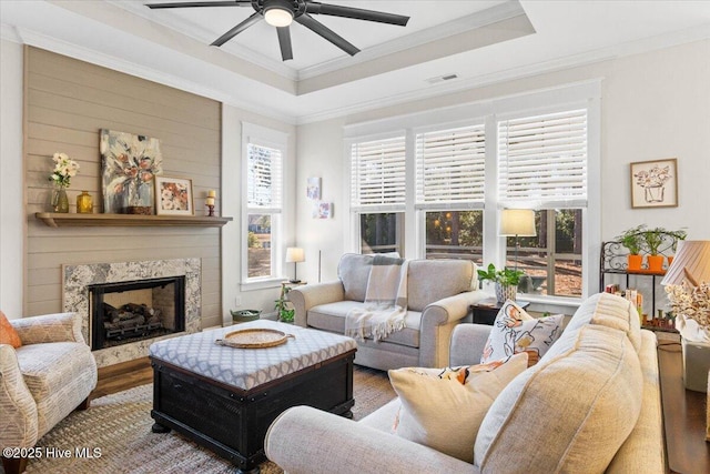 living area with ceiling fan, visible vents, wood finished floors, and a tray ceiling