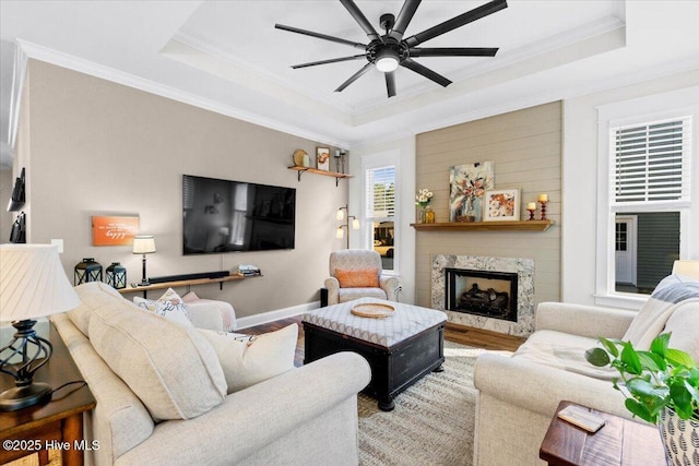 living area with ornamental molding, a ceiling fan, a tray ceiling, wood finished floors, and a high end fireplace