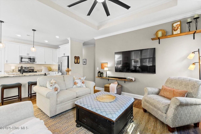 living area with baseboards, light wood-type flooring, ornamental molding, a raised ceiling, and a ceiling fan