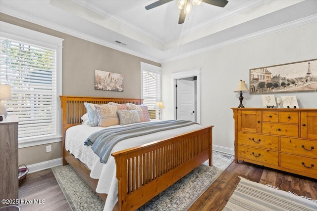 bedroom with a tray ceiling, wood finished floors, visible vents, and baseboards