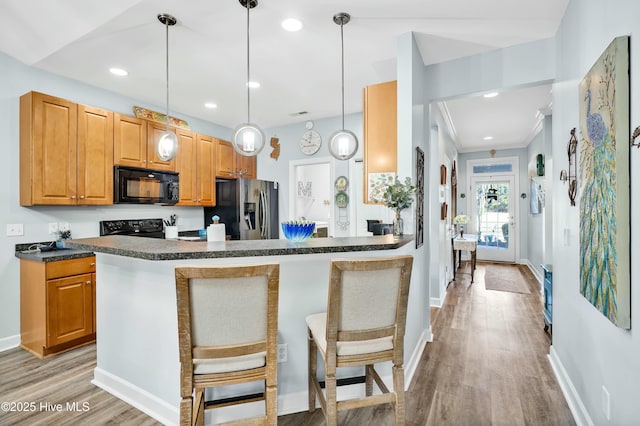 kitchen with light wood-style flooring, dark countertops, black appliances, and a breakfast bar