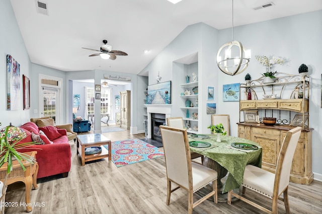 dining space featuring visible vents, built in shelves, light wood-style flooring, ceiling fan with notable chandelier, and a fireplace