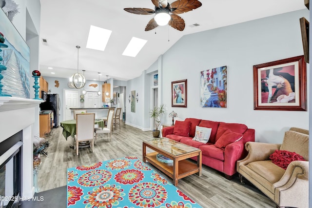 living room with visible vents, light wood-style flooring, a fireplace, ceiling fan, and lofted ceiling with skylight