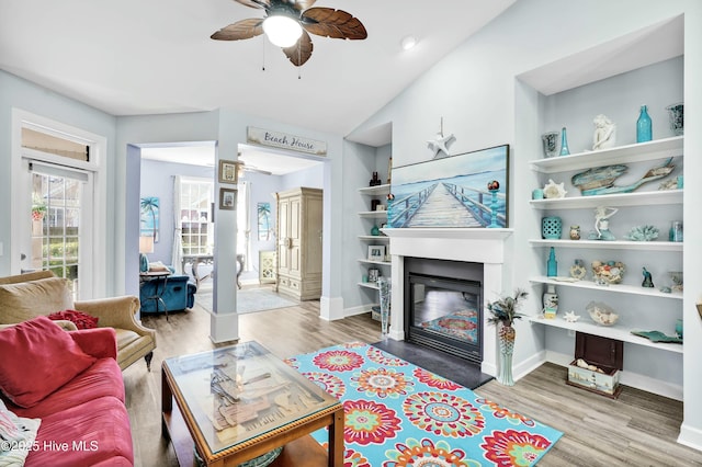 living area with a glass covered fireplace, baseboards, wood finished floors, and a ceiling fan