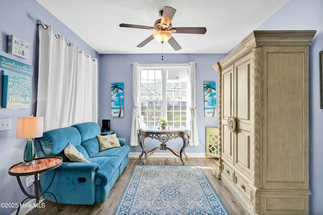 living area featuring wood finished floors, baseboards, and ceiling fan