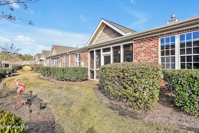 view of property exterior with brick siding, a yard, and a sunroom