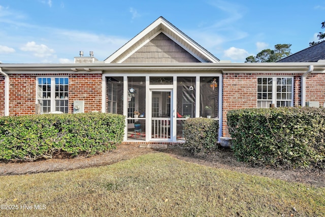 rear view of property featuring a yard, brick siding, and a sunroom