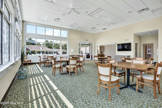 carpeted dining room with visible vents, baseboards, a towering ceiling, and a ceiling fan