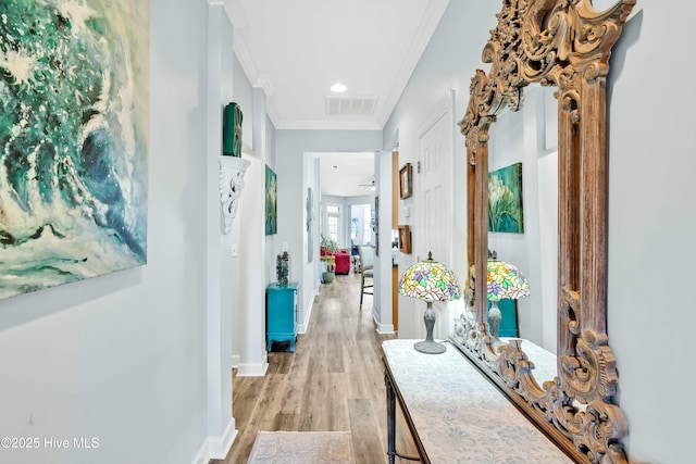 hallway featuring light wood-type flooring, baseboards, visible vents, and ornamental molding