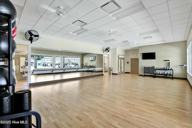 gym featuring light wood finished floors, visible vents, a paneled ceiling, and baseboards