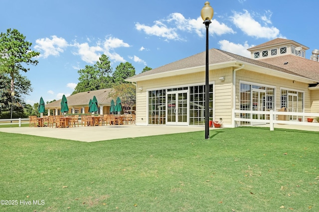 rear view of house with a lawn, a patio, and roof with shingles