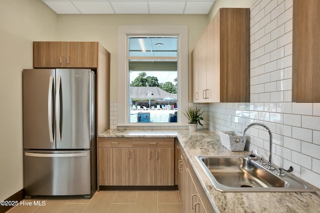 kitchen with a sink, decorative backsplash, brown cabinets, and freestanding refrigerator