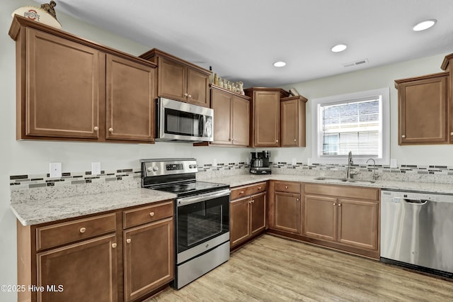 kitchen featuring a sink, light stone counters, recessed lighting, stainless steel appliances, and light wood-style floors