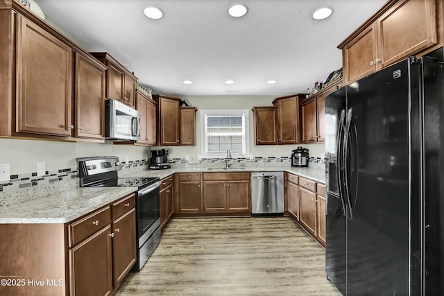 kitchen featuring a sink, recessed lighting, light wood-style floors, appliances with stainless steel finishes, and light stone countertops