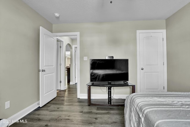 bedroom featuring a textured ceiling, wood finished floors, arched walkways, and baseboards